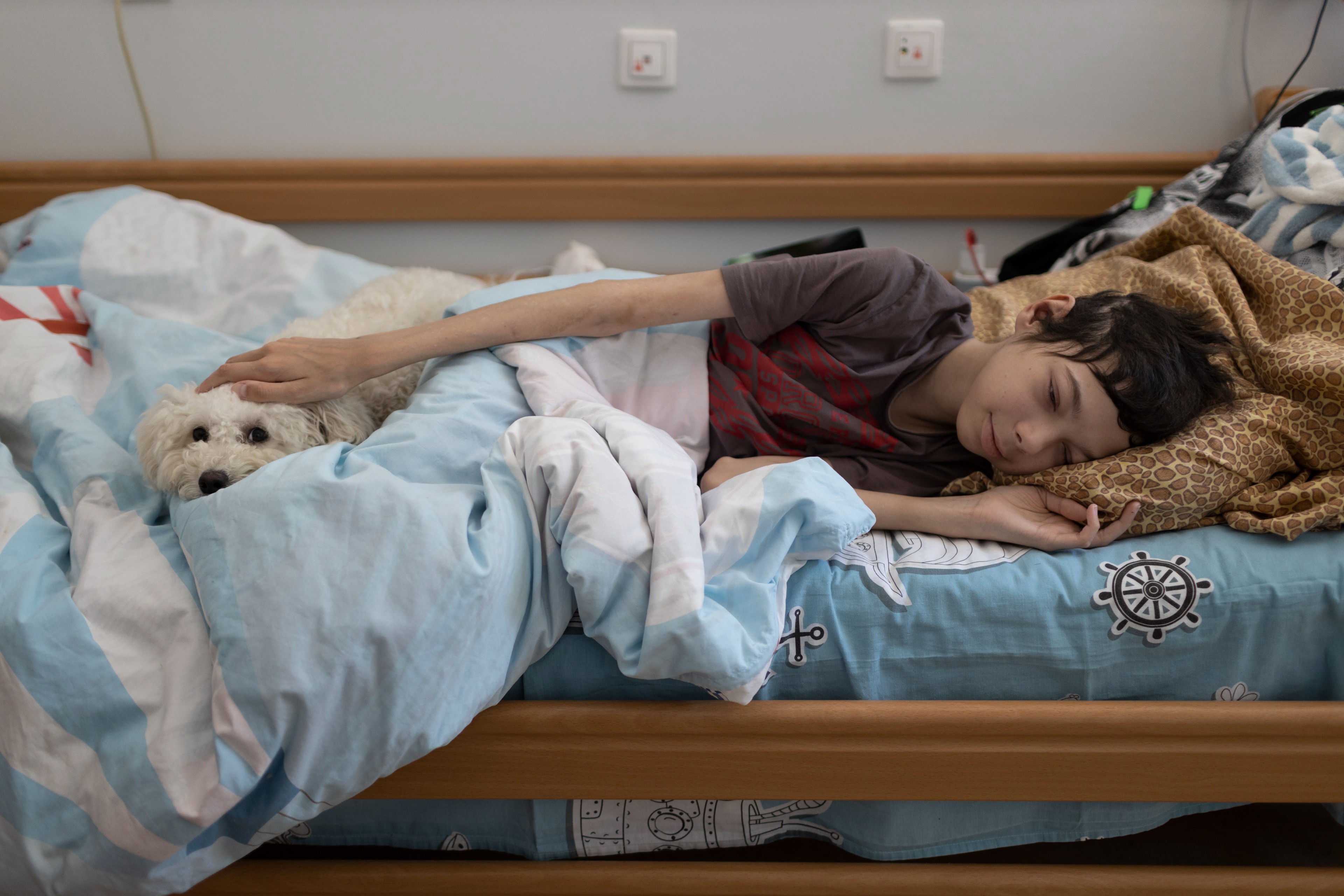 Alexey Veselov, a 16-year-old boy with advanced stage leukaemia, lays with fluffy Bichon Frise named Snezhok, or Snowflake on the bed at the House with the Lighthouse children’s hospice.