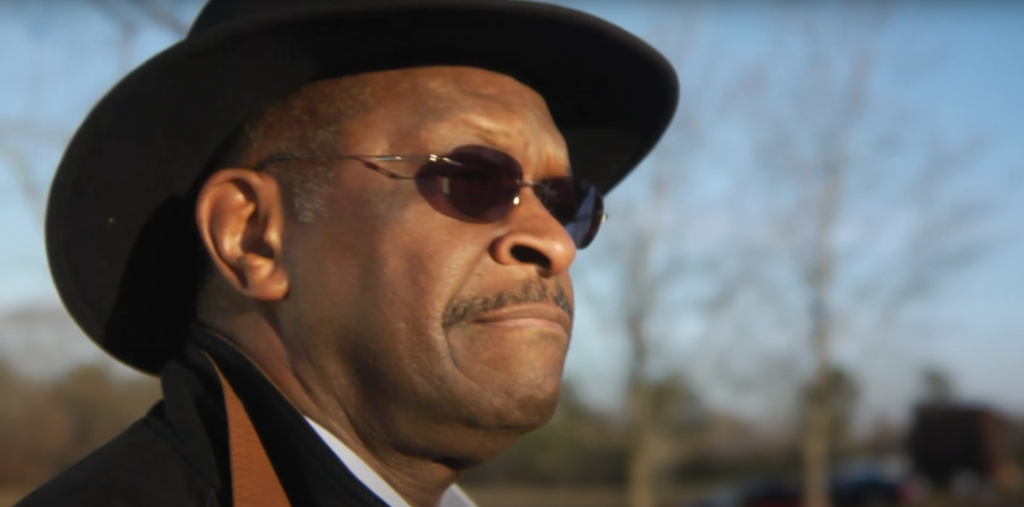 Herman Cain, dressed in all black, looking off into the distance.