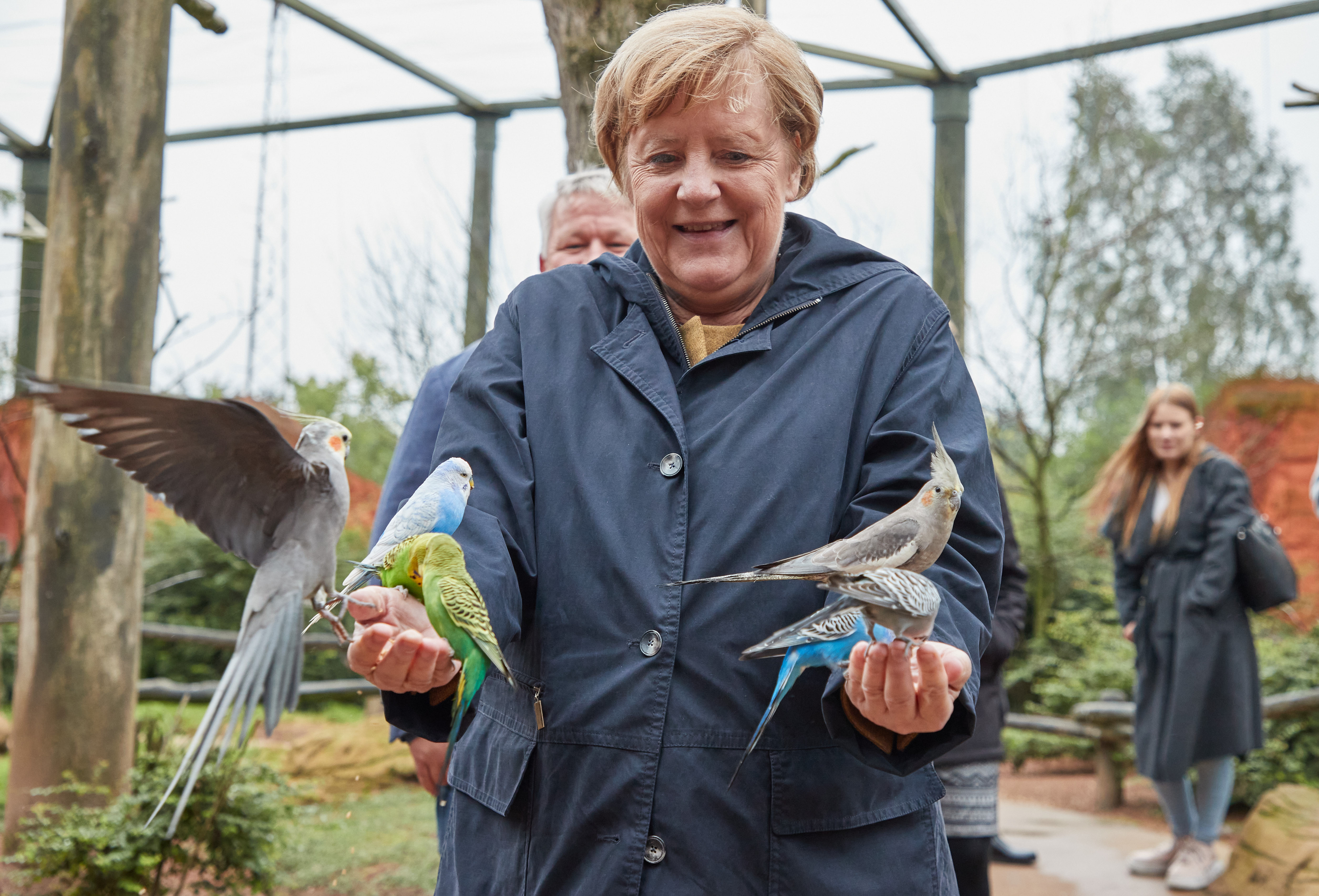 Angela Merkel hat mehrere bunte Vögel auf ihren Händen