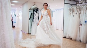 Die Autorin, die Brautkleider anprobiert um herauszufinden, ob sie heiraten möchte schreitet mit Brautkleid aus der Umkleide.