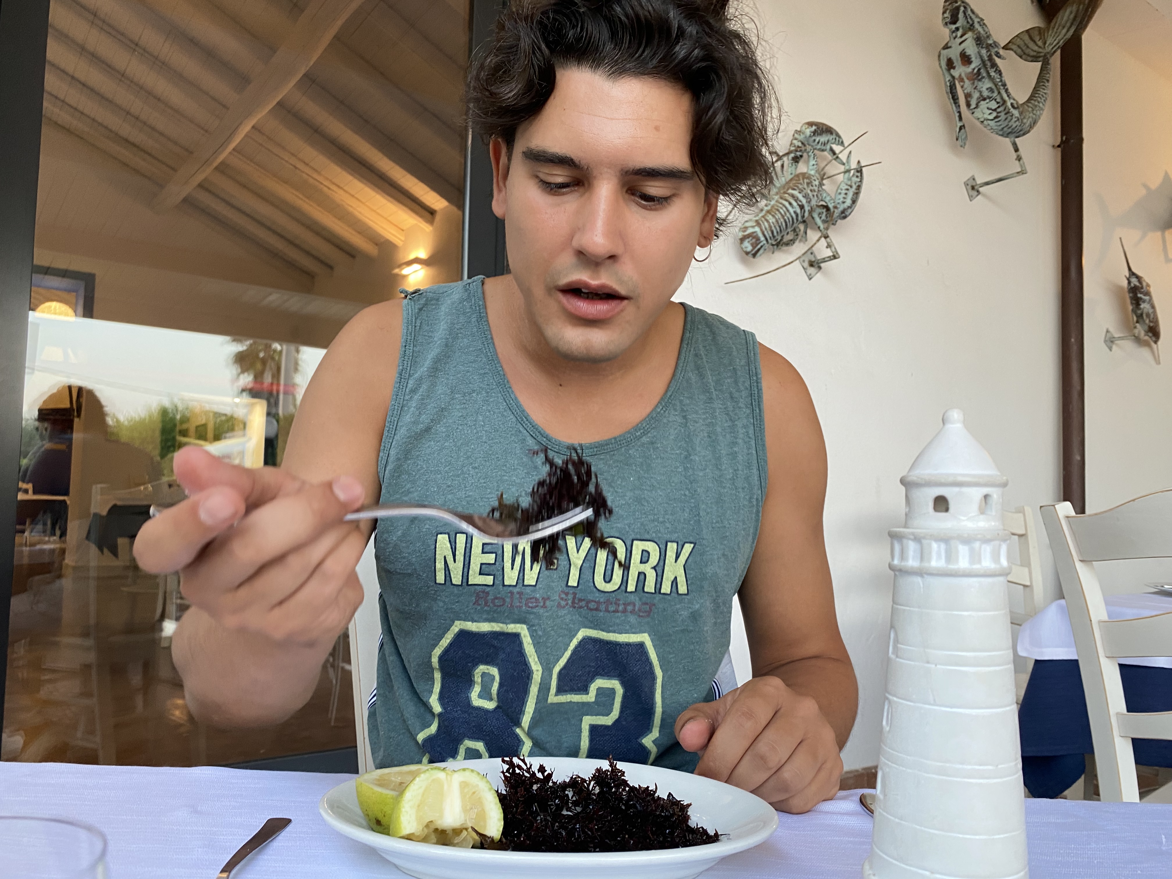 Mauru, Catania, Sicily – Man seated at a table decorated with a marine theme, about to put a forkful of red seaweed in his mouth.