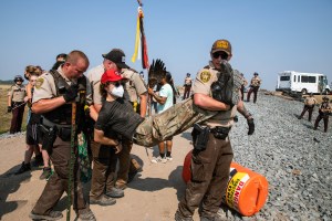 An oil pipeline protester is carried away by two police officers while handcuffed