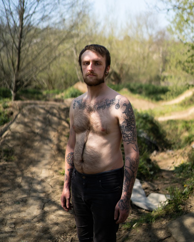 A dirt bike rider stands in the woods