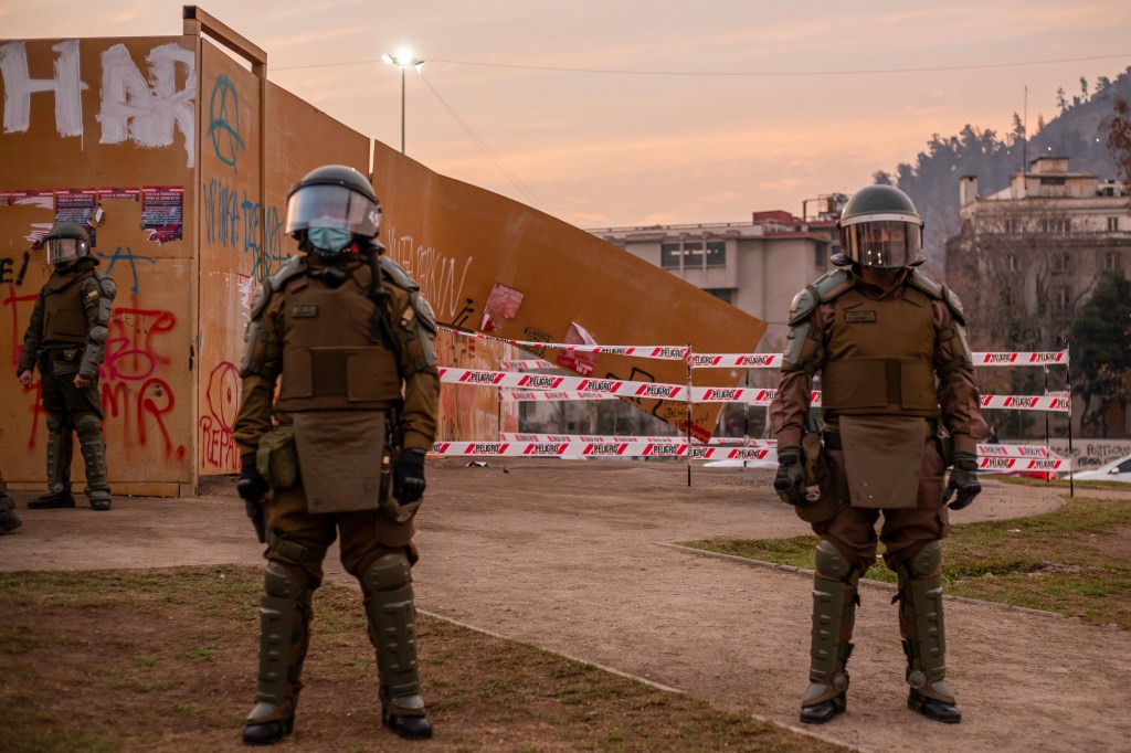 La policía antidisturbios chilena frente a un muro que fue rayado y parcialmente destruido durante una protesta para exigir la libertad de los presos políticos mapuche el 9 de julio de 2021 en Santiago, Chile. Foto de Claudio Abarca Sandoval/NurPhoto vía