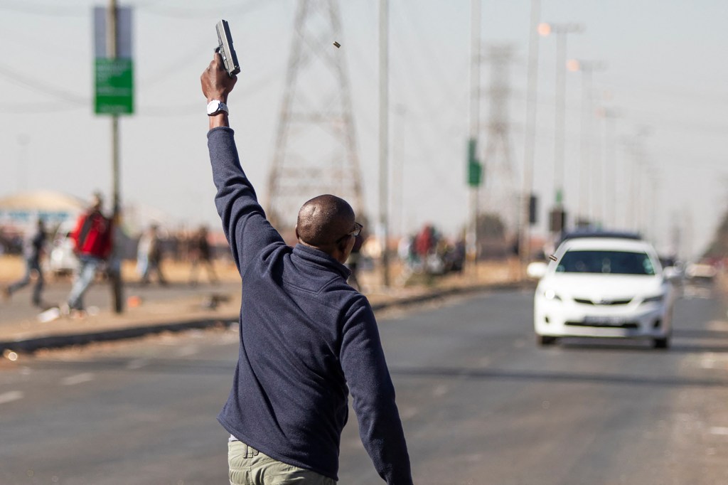 A man fires a handgun in the air to disperse a mob of alleged looters outside of the Chris Hani Mall in Vosloorus, on July 14, 2021. (Photo by GUILLEM SARTORIO/AFP via Getty Images)