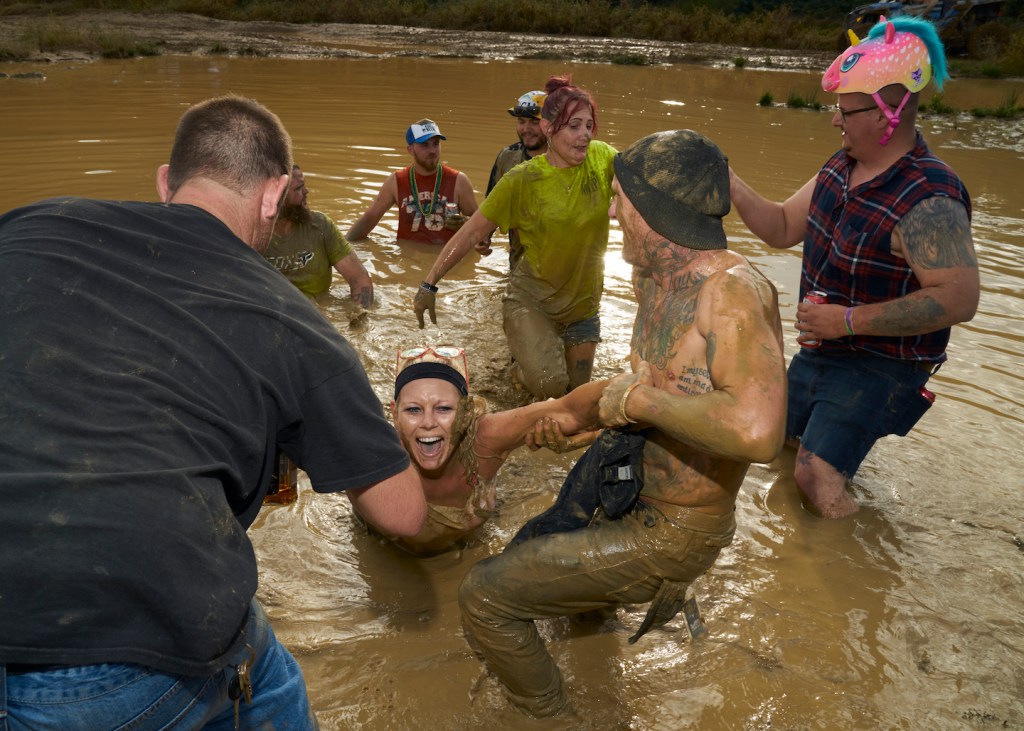 Mehrere junge Menschen stehen im kniehohen Wasser eines Schlammlochs, sie sind beim Redneck Rave, der verrücktesten Country-Party in den USA; wir waren dort, um das Chaos selbst zu erleben