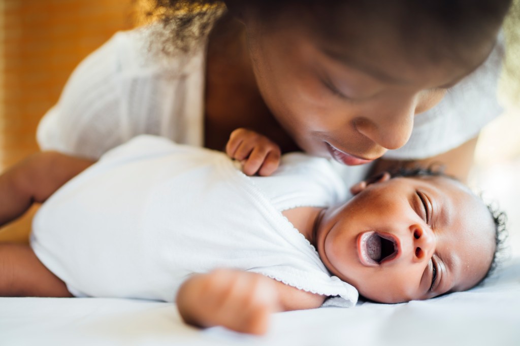 Close-up of mother looking at newborn daughter yawning while lying on bed