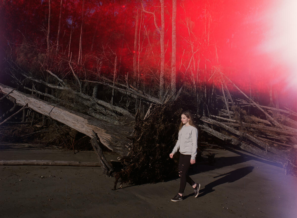 Raeden, 13, walks past a dead tree that has been dislodged due to erosion on a beach in Batemans Bay, Australia. Image: Matthew Abbott / Save the Children