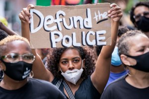 An African American protester wears a mask and holds a homemade sign that says, "Defund the Police" as they perform a peaceful protest walk across the Brooklyn Bridge.