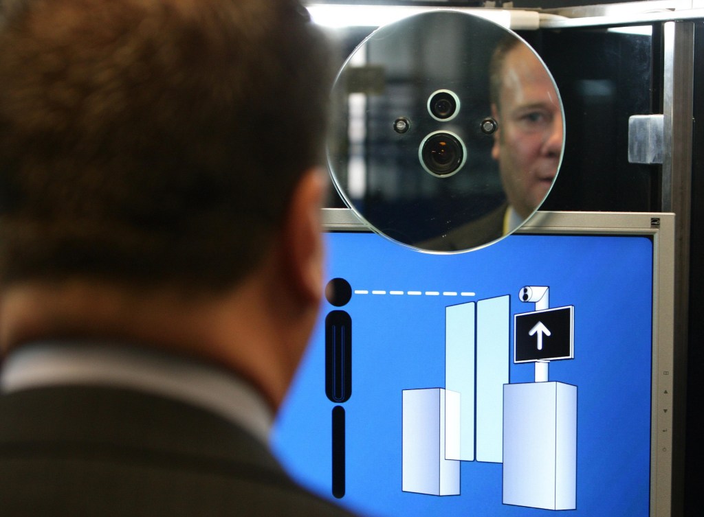 A man an airport stands in front of a facial recognition camera and a digital display with visual instructions