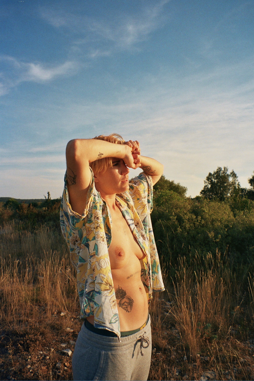 Of Manifesto, Belgium, porn - A woman in an open shirt stands in a patch of scrubby plants and bushes.