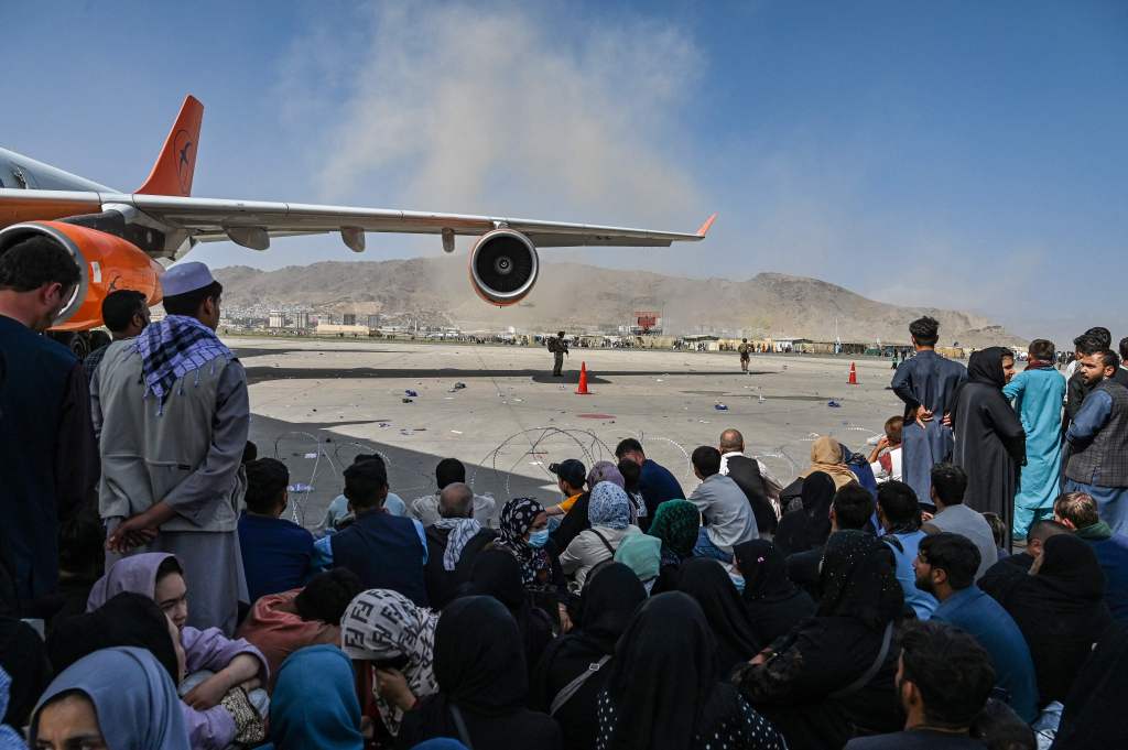 Afghan people sit as they wait to leave the Kabul airport in Kabul on the 16th of August. Photo: WAKIL KOHSAR/AFP via Getty Images​