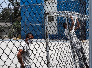 zwei junge Männer mit weißen T-Shirts und Mund-Nasen-Bedeckung hinter einem Zaun, einer macht Pull-ups an einem Fußballtor. In Mexiko werden immer mehr junge Menschen von den Kartellen angeheuert