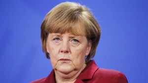 Angela Merkel steht vor blauem Hintergrund und sieht grimmig aus wie immer, wofür die Autorin sie liebt.