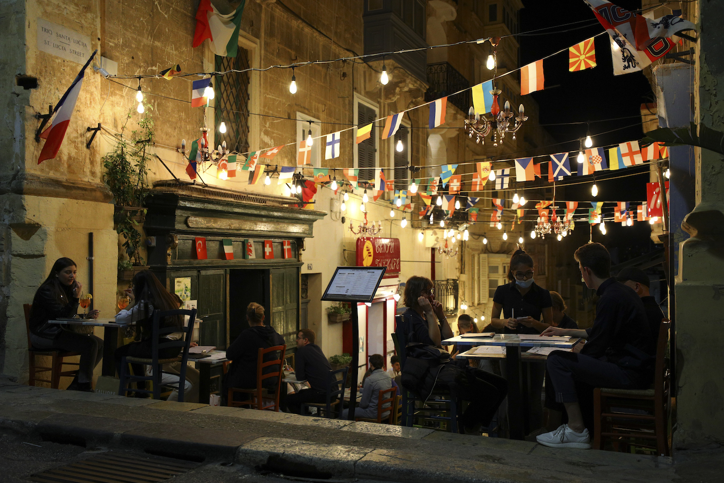 A waiter wearing a protective mask accepts an order from tourists at a street cafe in Valletta