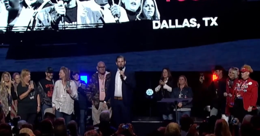 Michael Flynn, Roger Stone, and Eric Trump stand on stage at the ReAwaken America conference in Dallas.