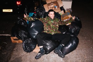 A smiling man falling in a pile of bin bags on New Year's Eve