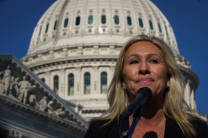 Marjorie Taylor Green stands in front of the Capitol Dome; she's smirking in front of a microphone.