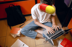 A university student sat on the floor with his laptop with a study drug superimposed on his face