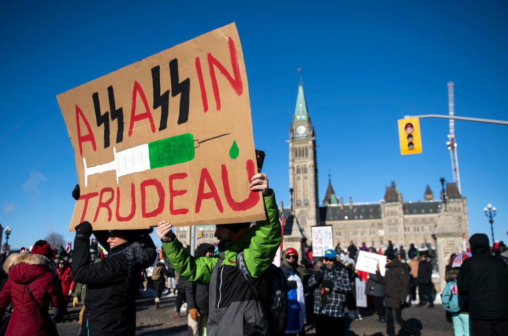 People hold a sign against Prime Minister Justin Trudeau and vaccinations during a rally against COVID-19 restrictions on Parliament Hill on Saturday.