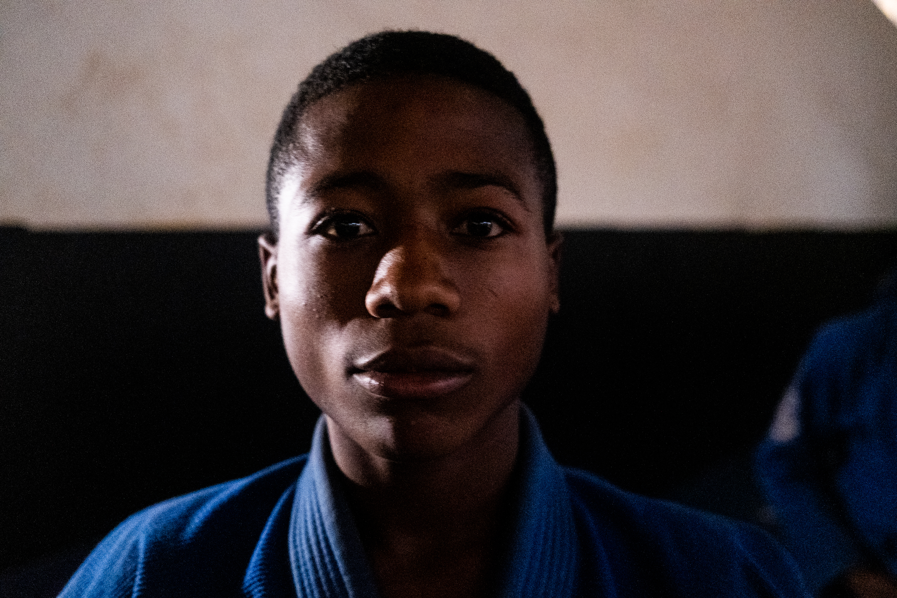 Foundation Ngannou, Batié, Cameroon – Kelvin, teenage kid with short hair wearing a blue jiu jitsu suit and looking straight at camera.