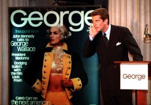 Photo shows John F. Kennedy Jr. with his hand cupped to his ear at a lectern that reads George. Behind him is a magazine cover showing Cindy Crawford dressed as George Washington.