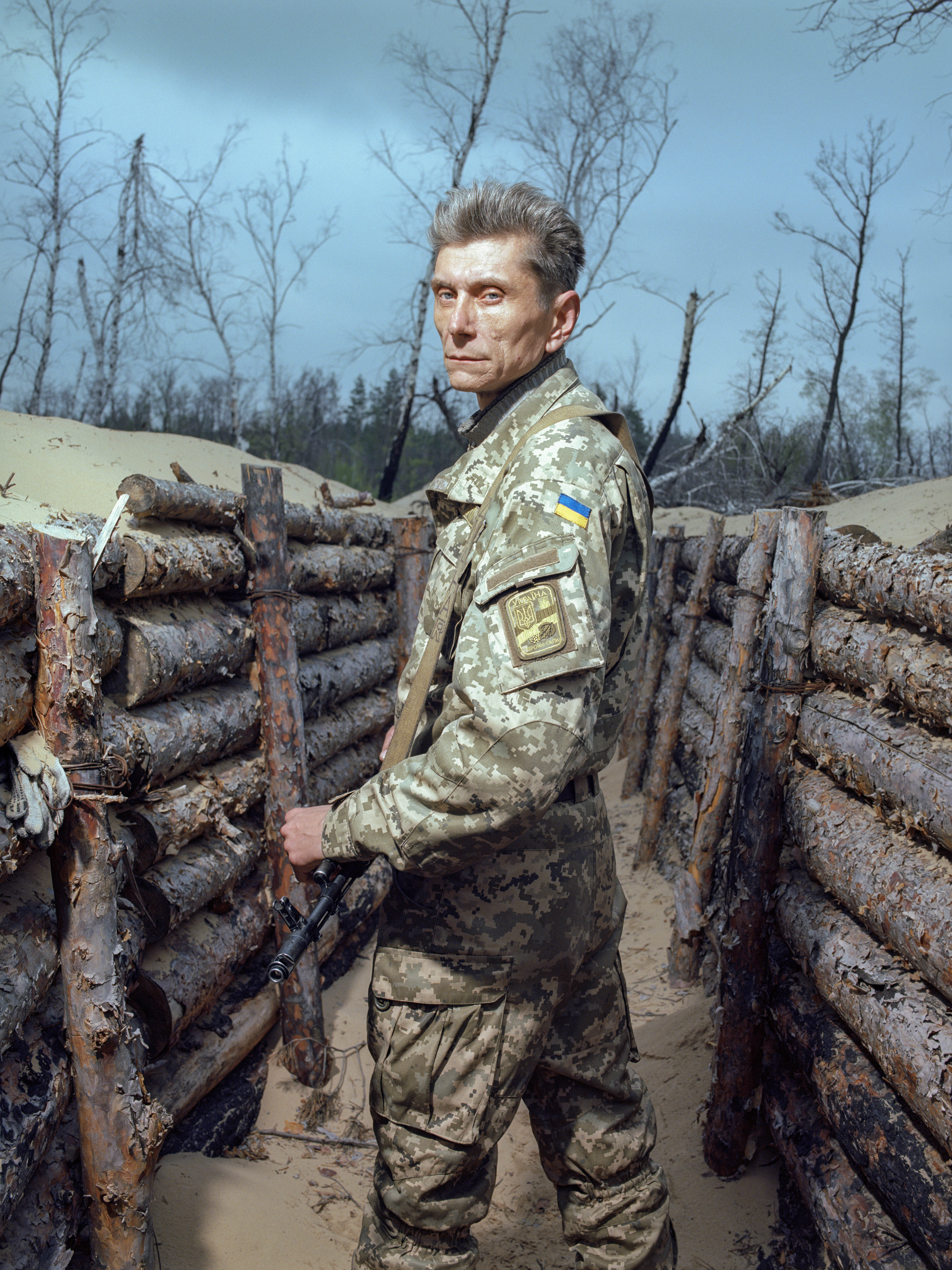 Ein bewaffneter ukrainischer Soldat steht in einem mit Holz befestigtem Graben und blickt über die Schulter in die Kamera