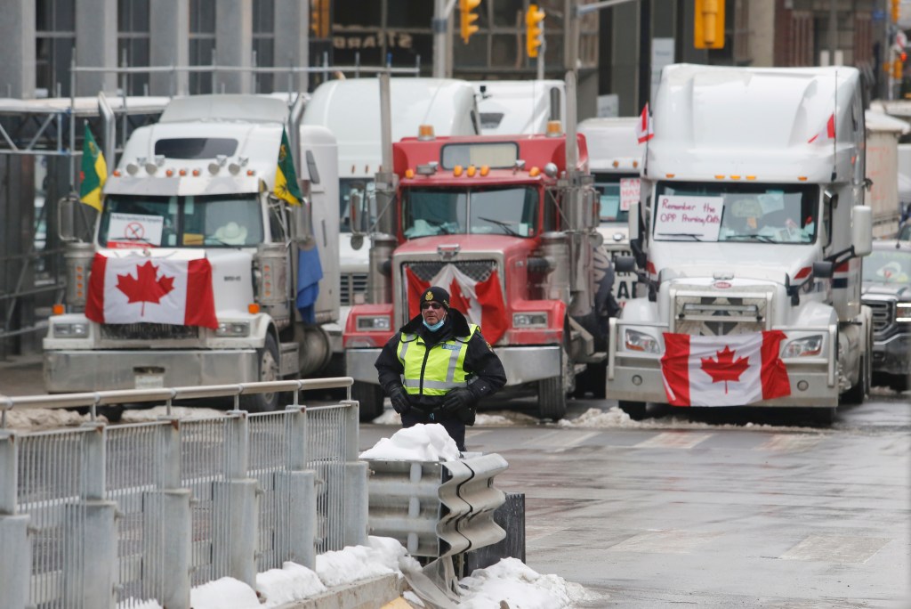 A police member stands in front of trucks blocking downtown streets as a rally against COVID-19 restrictions, which began as a cross-country convoy protesting a federal vaccine mandate for truckers, continues in Ottawa, on Wednesday, February 9, 2022.