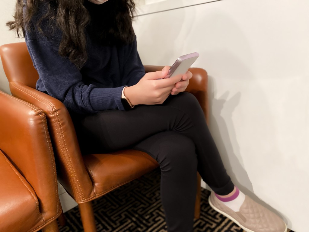 A teenage girl sitting on a chair looking at her phone.