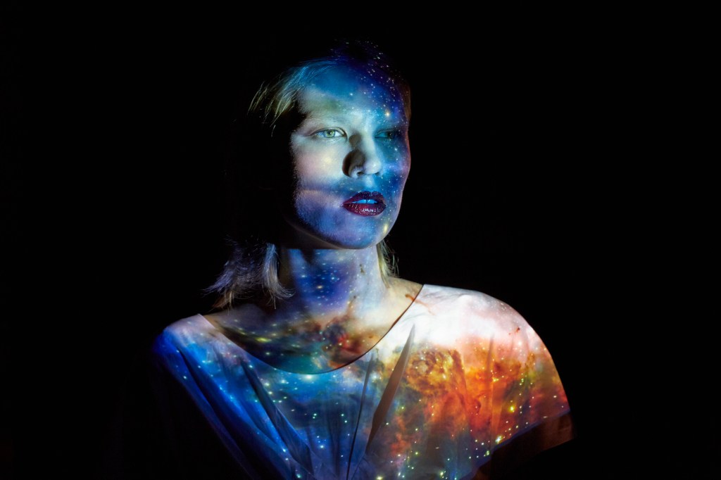 Woman stand in the dark with universe reflected on her body.