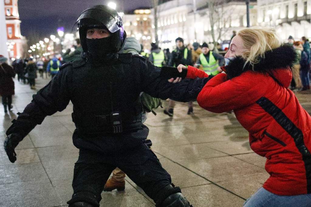 Ein Polizist mit Helm und Schutzausrüstung zerrt auf einem Platz eine blonde Frau am Arm, viele Menschen in Russland sind gegen die Invasion der Ukraine.