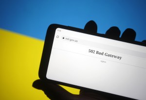 A hand holding a smartphone displaying a "502 Bad Gateway" error for a Ukrainian website, with a blue and yellow Ukrainian flag in the background