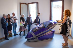 Death, assisted suicide, health - Photograph of a group of people stood around a purple assisted suicide capsule.