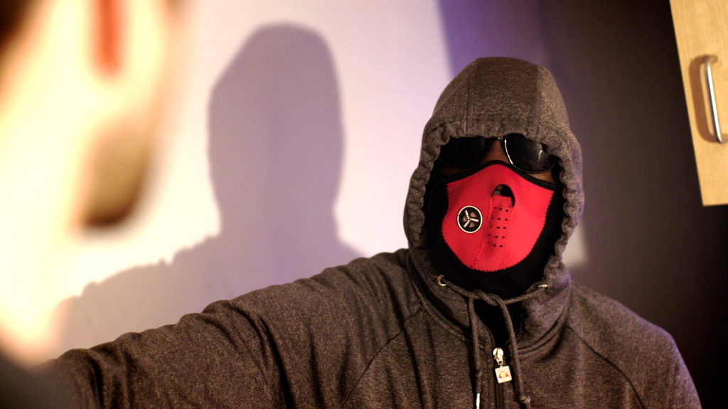 A drug trafficker wearing a hood, sunglasses and a red mask.