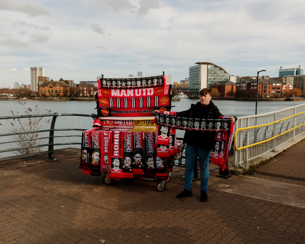 A Manchester United merch seller holding a scarf.