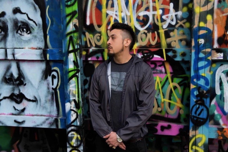 Reggaeton rapper William Davila AKA Guala standing against a graffiti covered wall.