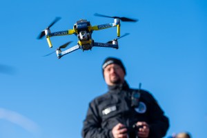 A flying quad rotor drone is controlled by a police officers