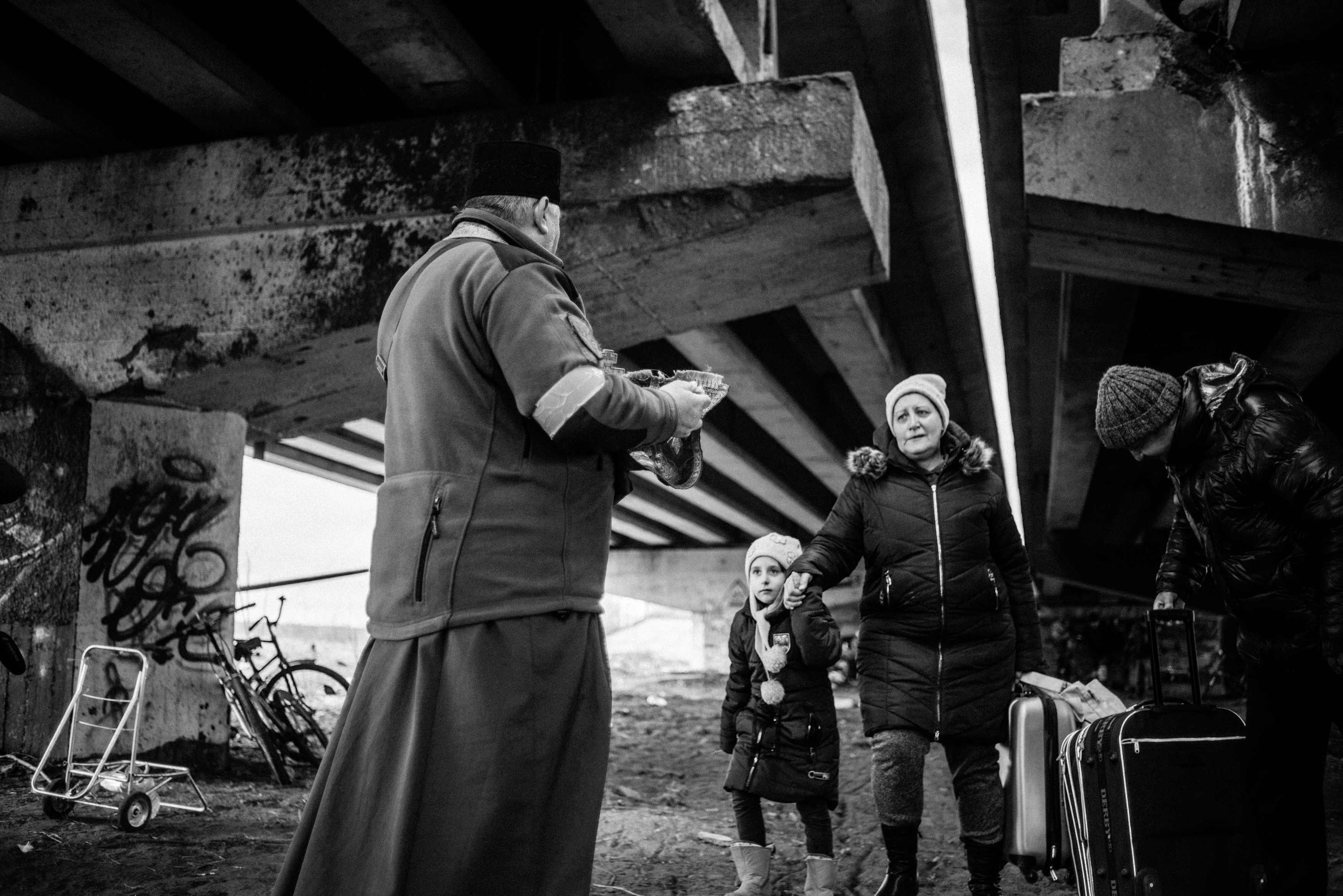 A priest takes communion with a family of people crossing the destroyed bridge connecting Irpin and the road to Kyiv