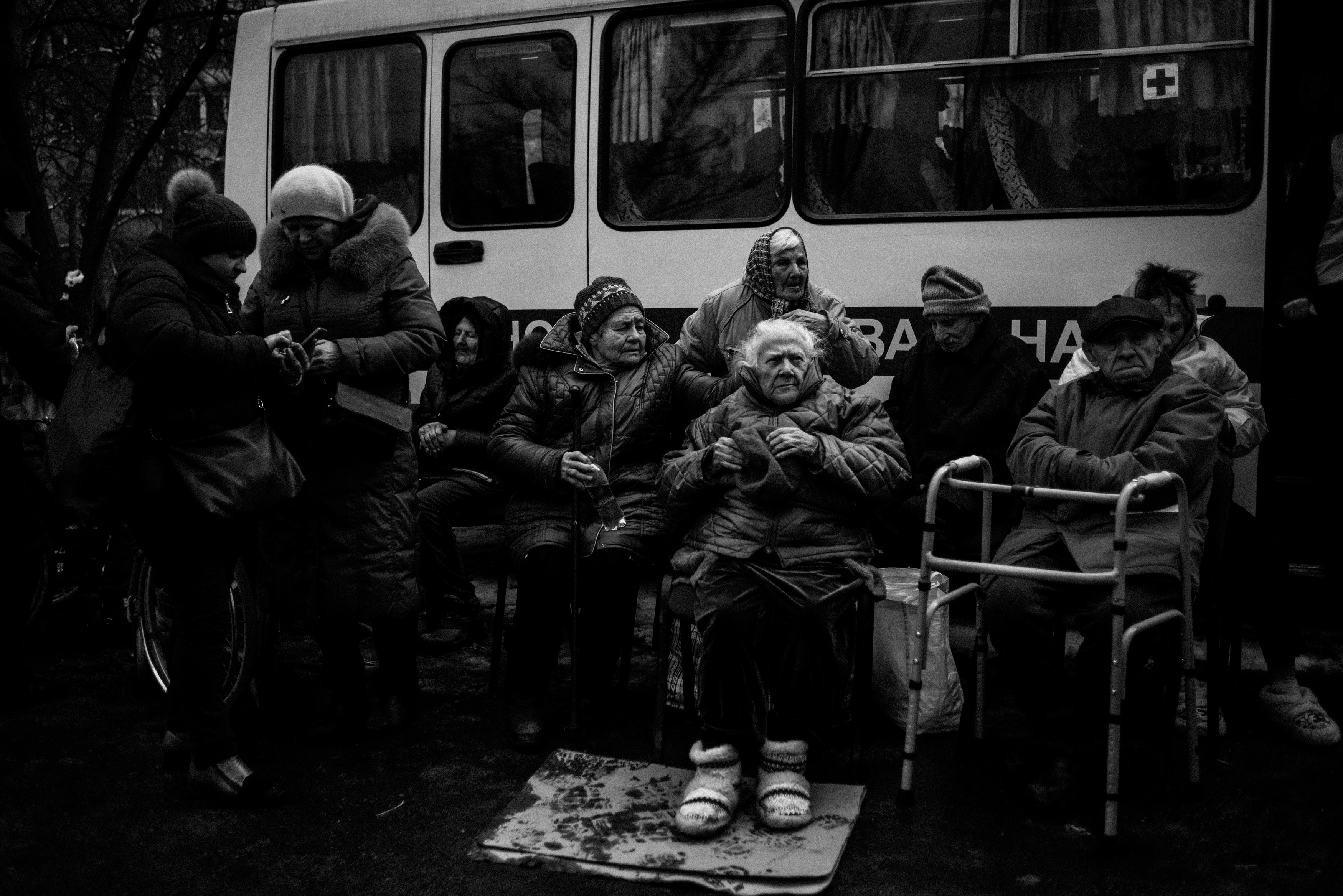 Older people sit by a bus after being evacuated from Irpin.