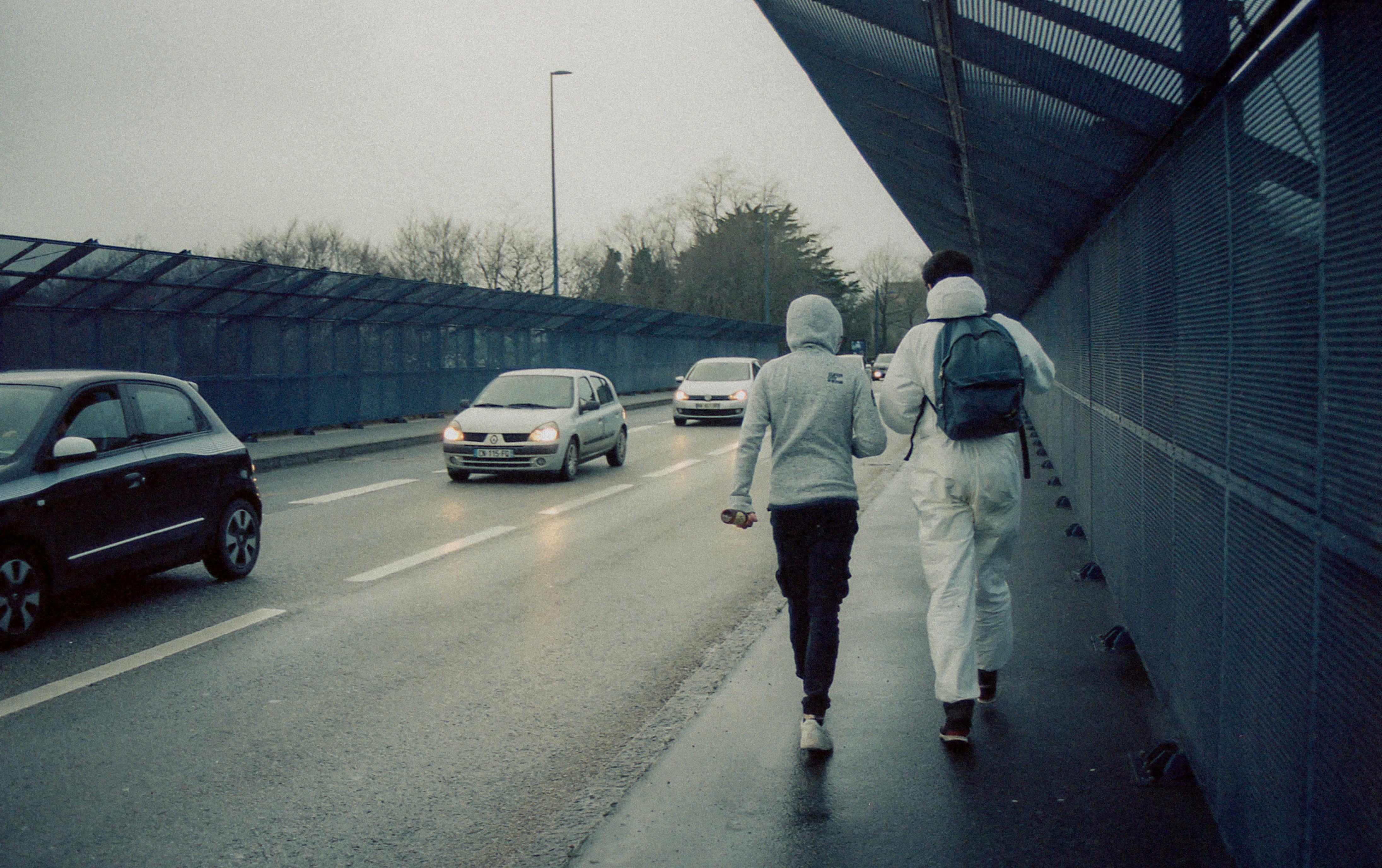 Mushary, France, hobbies – Photograph of two men (one in a grey hoodie, the other in a white boiler suit) walking over a bridge with their backs to the camera.