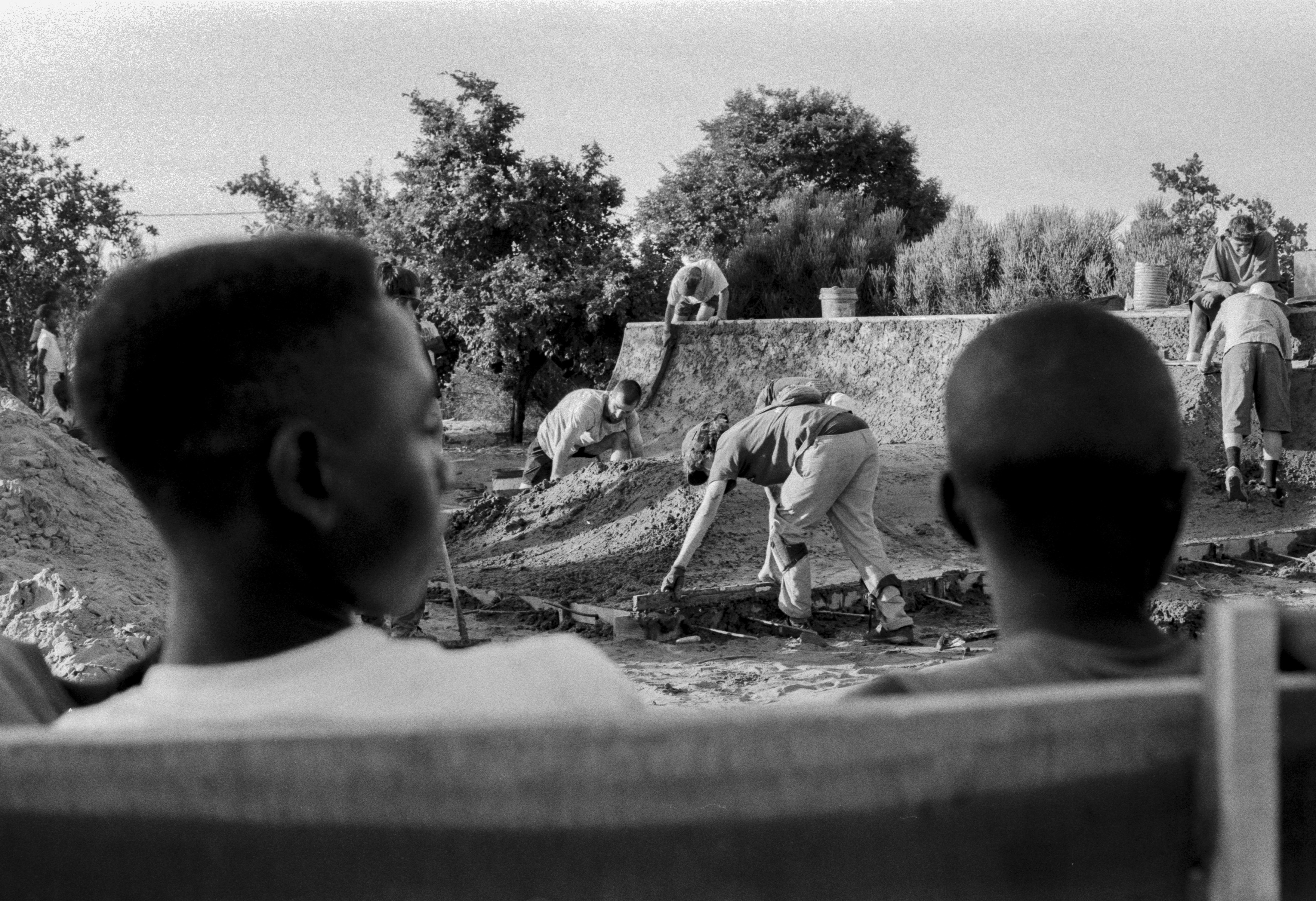 Africa, skateboarding, Jonas Camps - Black and white photo of two boys watching a group of men doing construction work.