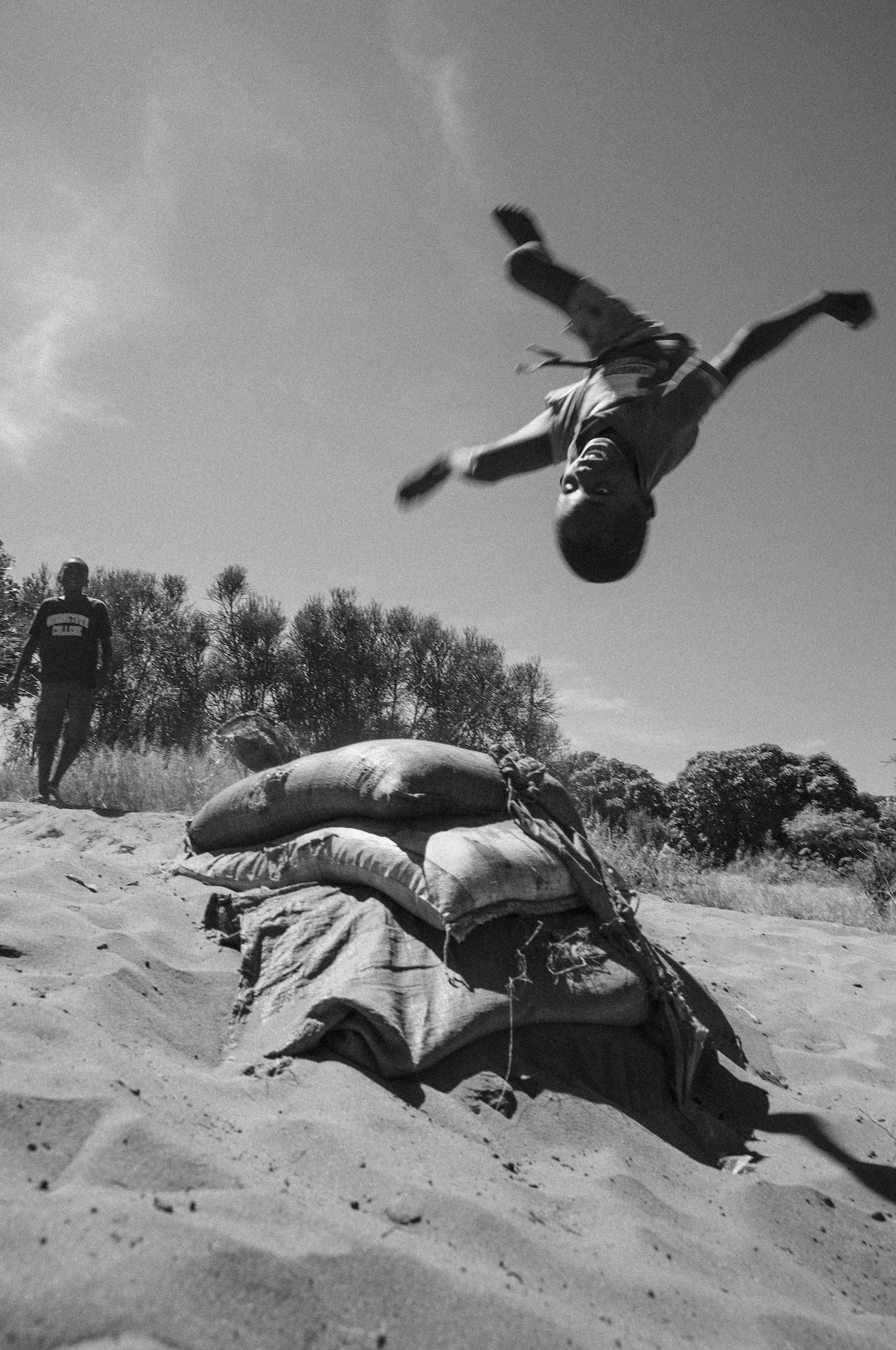 Africa, skateboarding, Jonas Camps - Black and white photo of a boy in mid-air, flipping over a pile of sandbags.