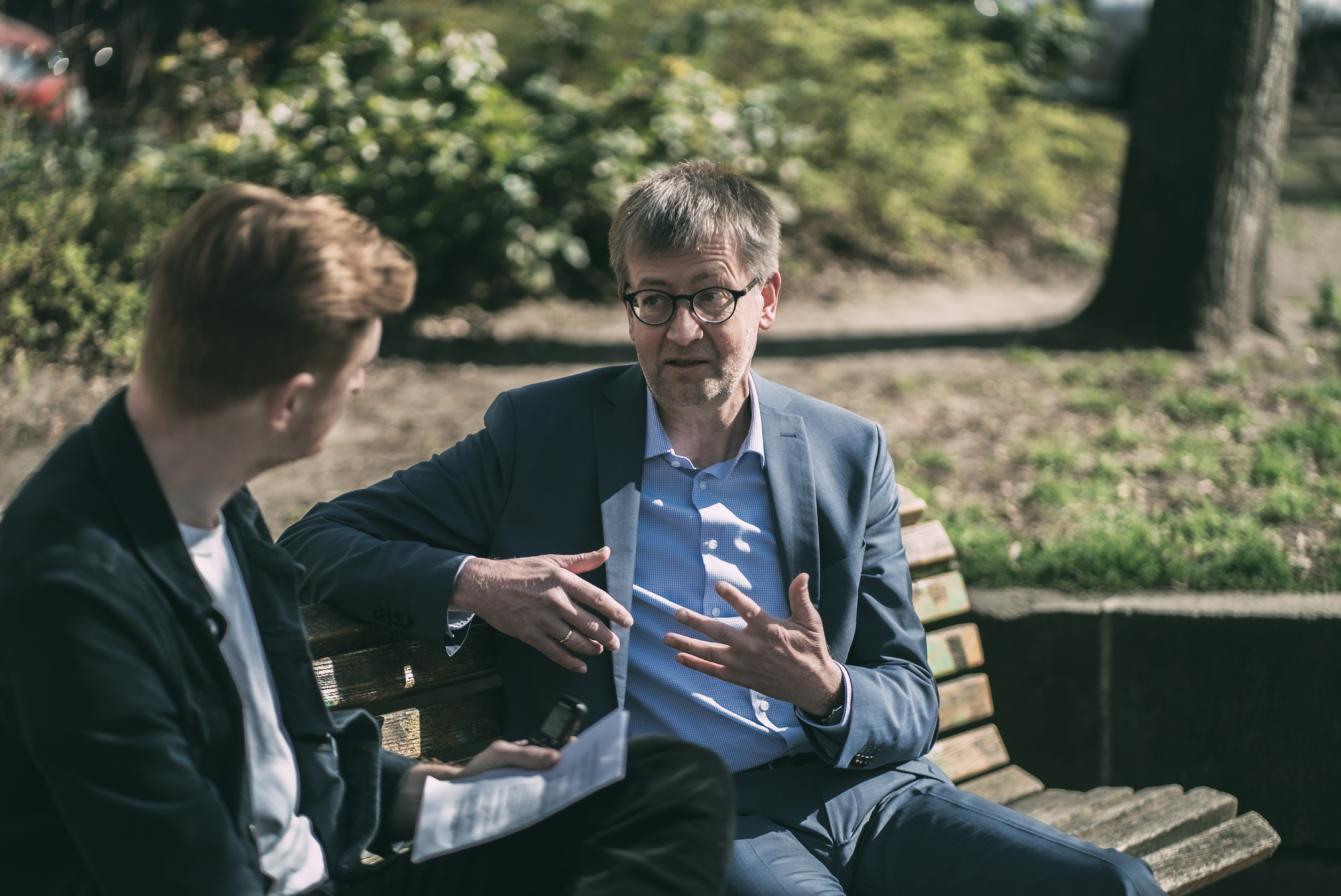 Der Drogenbeauftragte Burkhard Blienert, ein Mann mittleren Alters mit grauen Haaren und Brille, sitzt im Interview auf einer Bank und spricht über die Legalisierung von Cannabis