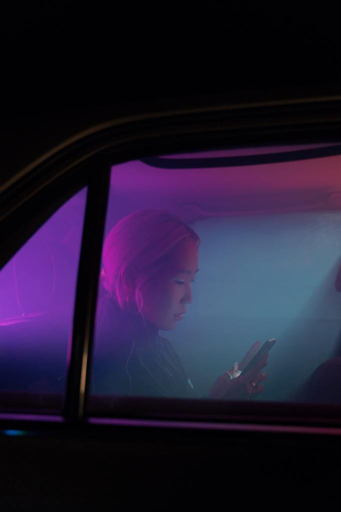 A woman sits in a car reading her phone. Photo by cottonbro from Pexels