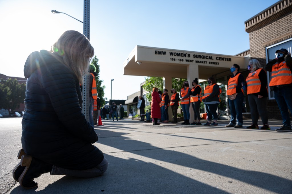 A pro-life demonstrator kneels in front of a line of volunteer clinic escorts in front of the EMW Women's Surgical Center, an abortion clinic, on May 8, 2021 in Louisville, Kentucky.