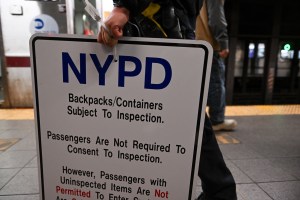 NYPD officer carries a “backpacks subject to investigation” sign.