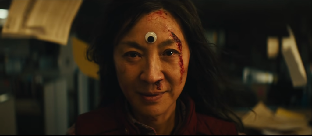 A screenshot of Michelle Yeoh with a googly eye on her forehead from Everything Everywhere All At Once