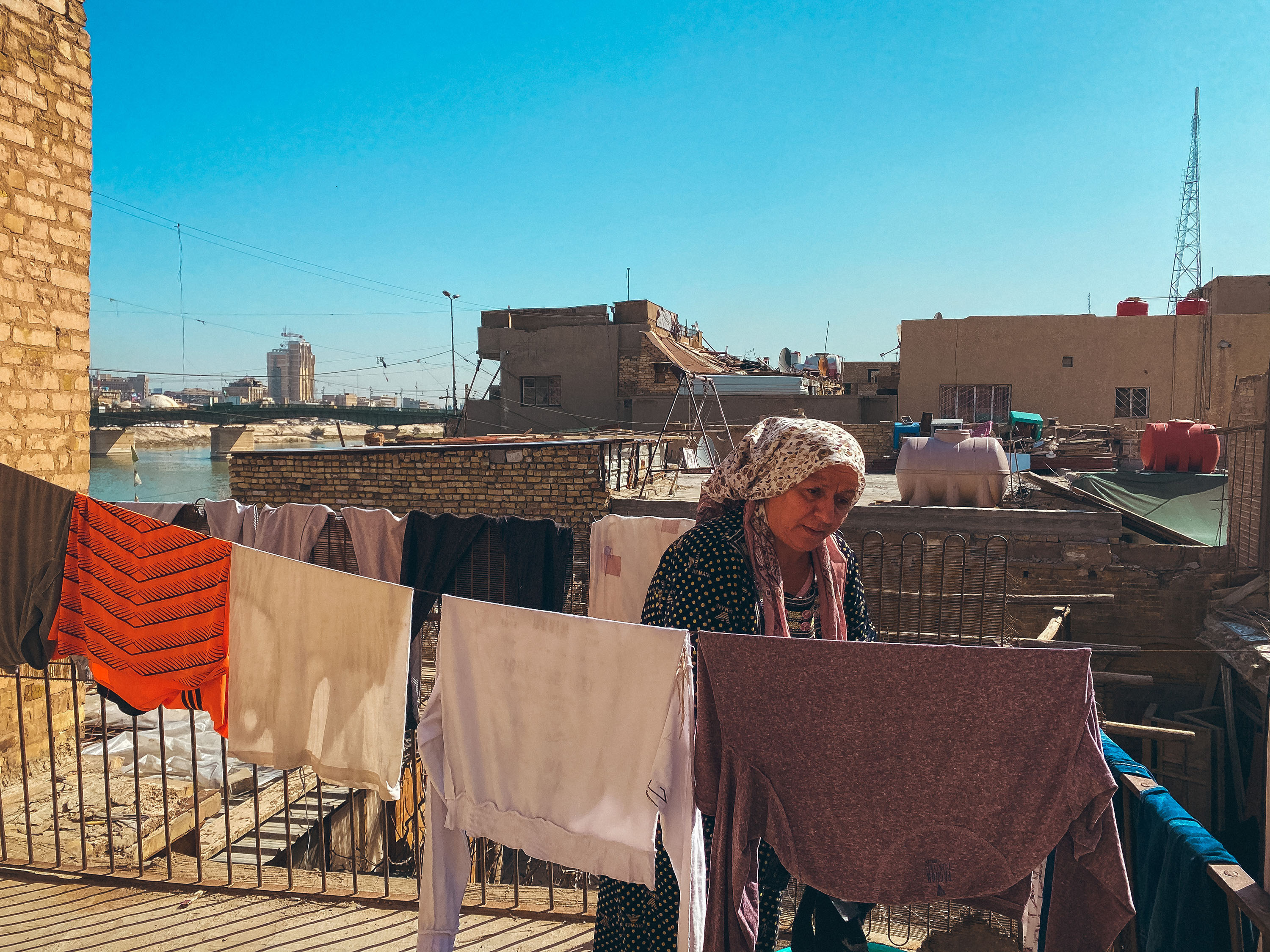 Al-Shawaka district, Baghdad – woman wearing a long polka-dotted dress and a floral headscarf, hanging clothes on some clothing lines on her rooftop.