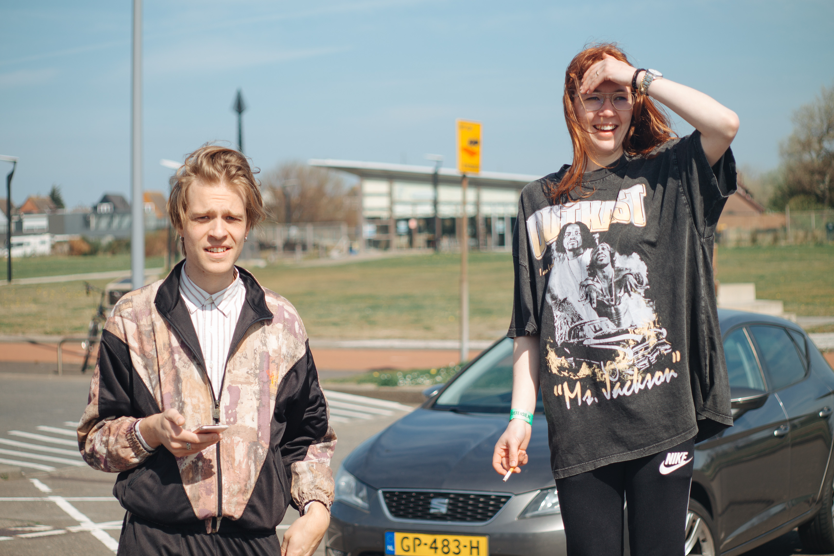 Army recruitment, Fort 1881 – the author (left) and luna, a girl with long red hear wearing a band tee and leggins smoking a cigarette in front of a parking lot.