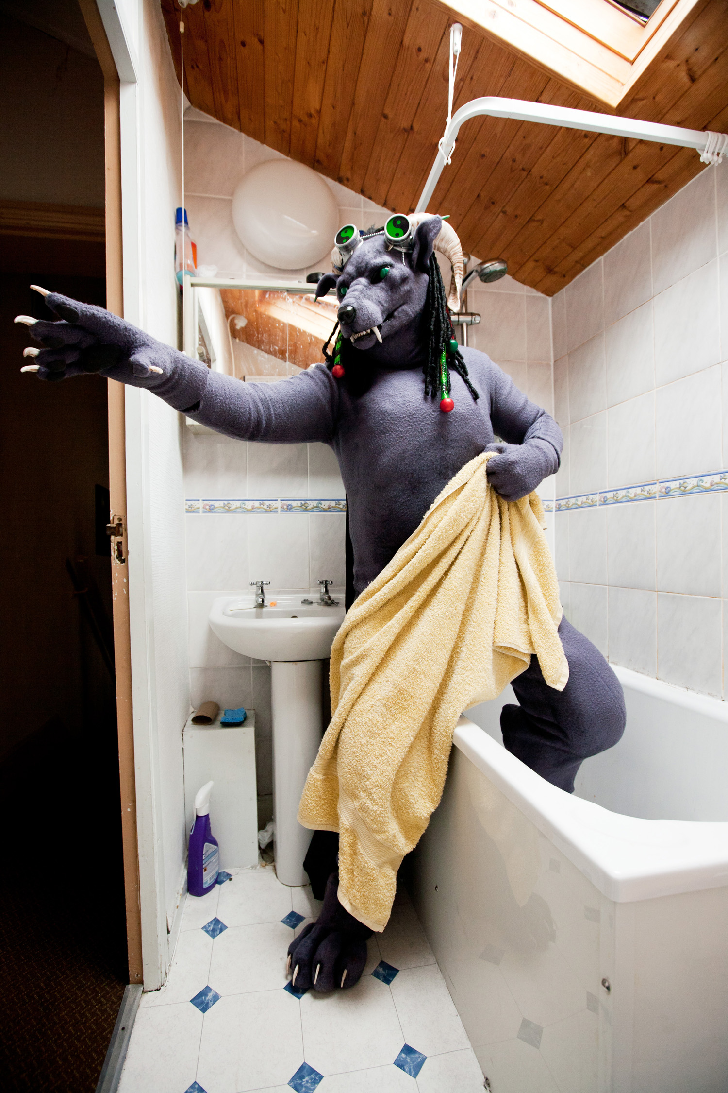 A fursuiter dressed as a gargoyle steps out from the shower holding a towel.